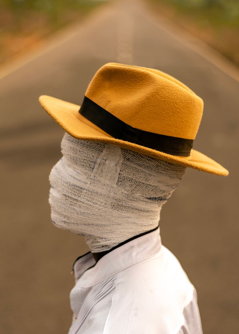 A mysterious figure with a bandaged head wearing a hat stands on a road.