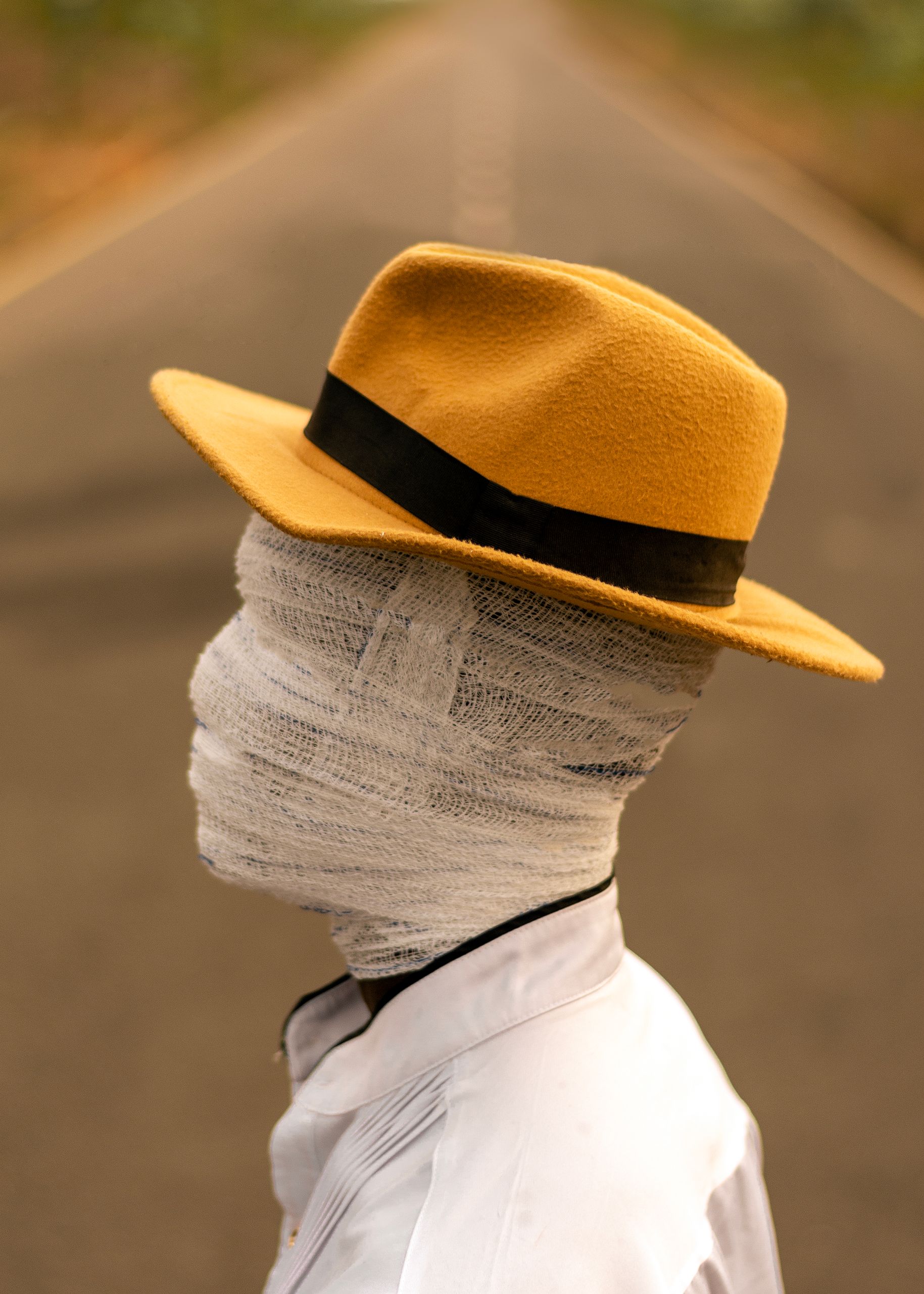 A mysterious figure with a bandaged head wearing a hat stands on a road.