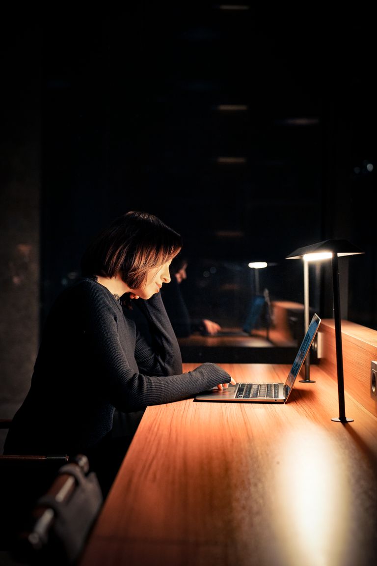 Focused woman using laptop at night in a dimly lit workspace, emphasizing concentration and technology.