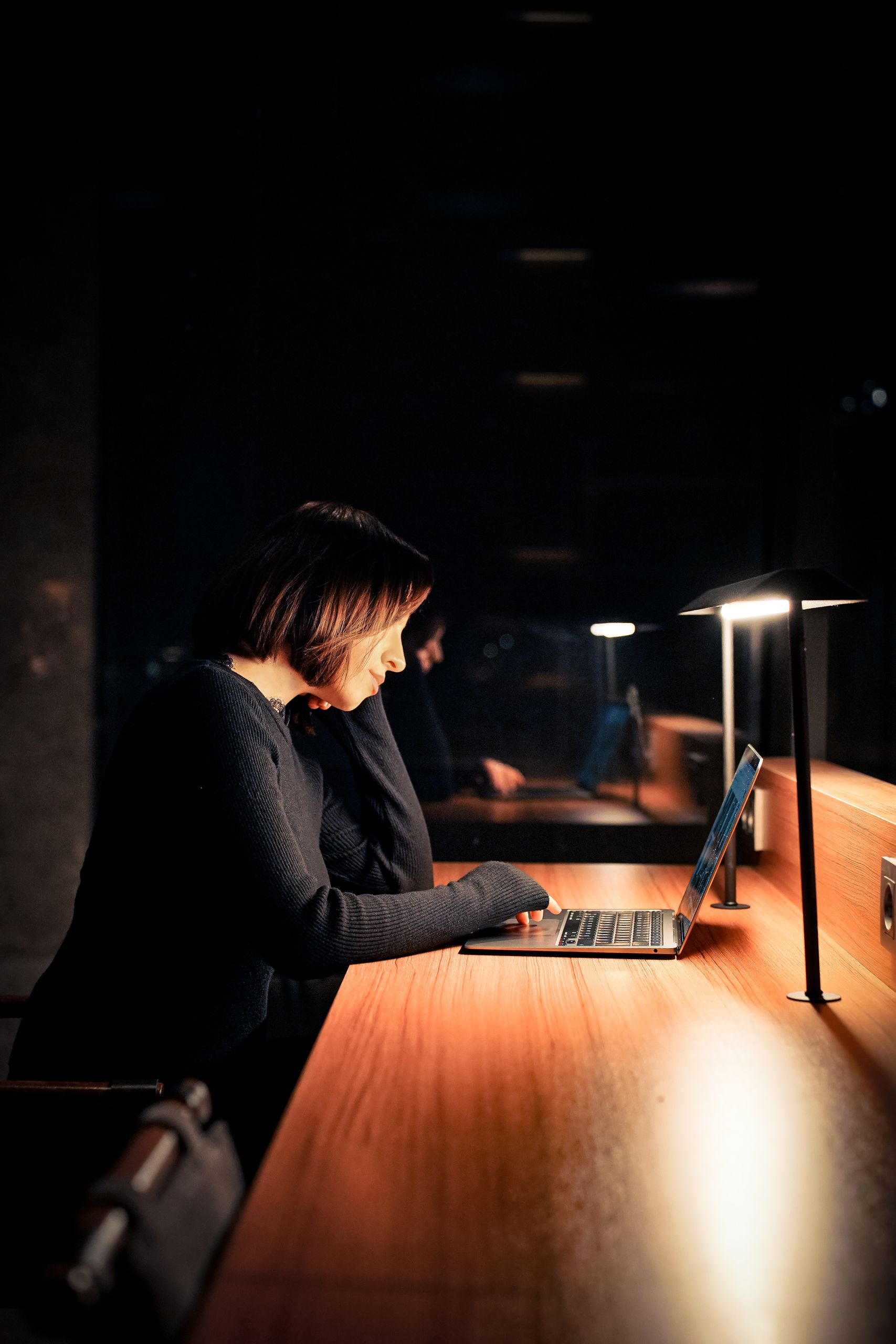 Focused woman using laptop at night in a dimly lit workspace, emphasizing concentration and technology.