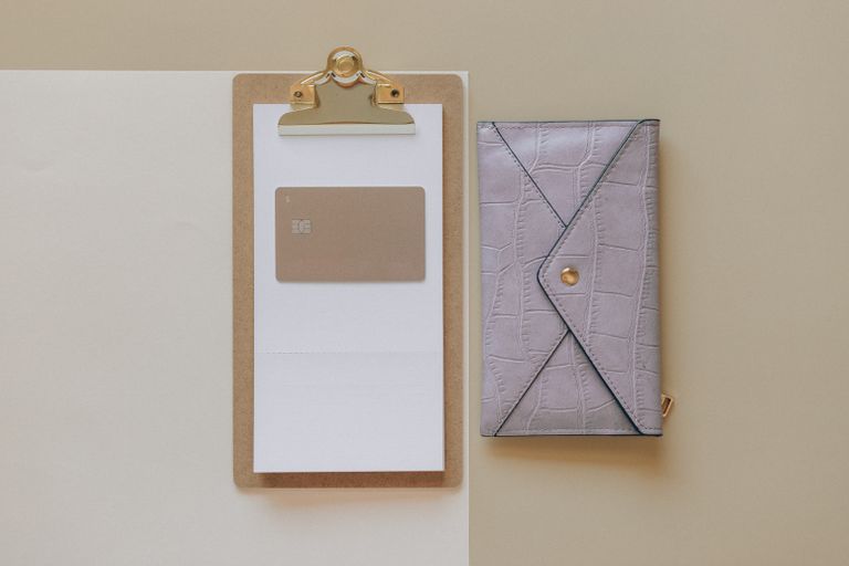 Simple flat lay of a clipboard with a card and a stylish wallet on a neutral background.