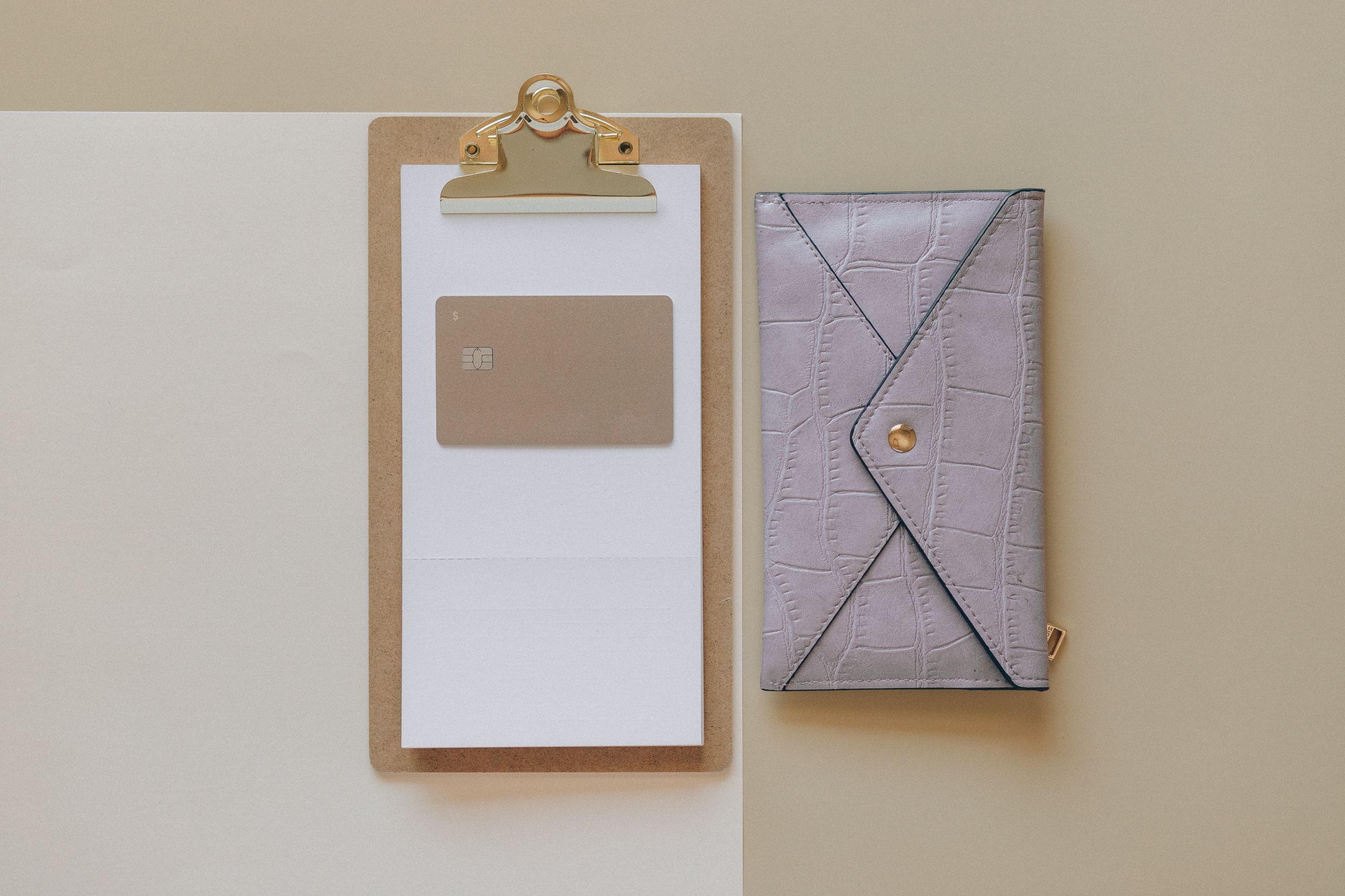 Simple flat lay of a clipboard with a card and a stylish wallet on a neutral background.