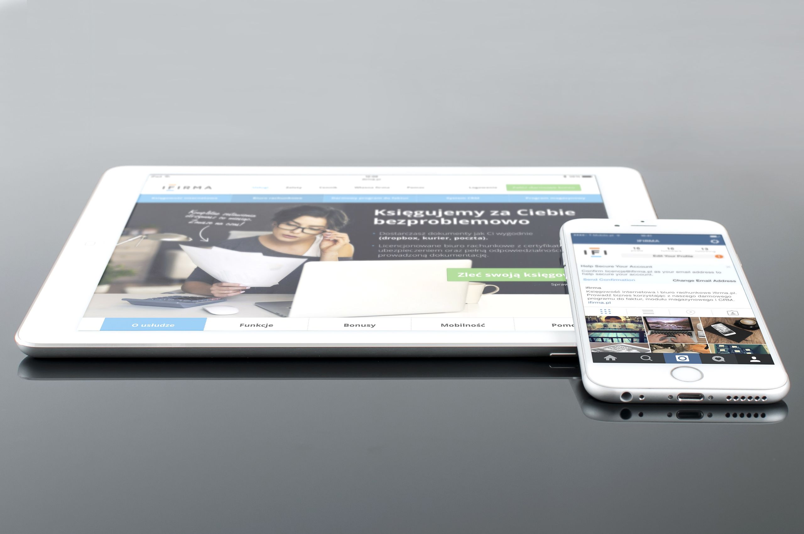 Modern tablet and smartphone displaying web content on a reflective surface, highlighting technology and connectivity.