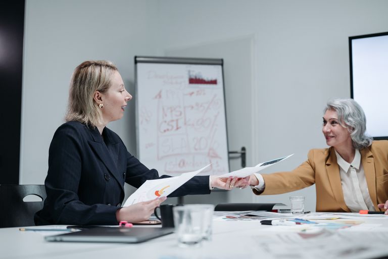 Two businesswomen exchanging documents during a meeting in a modern office.